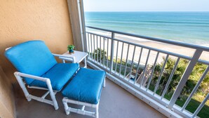 A balcony with white chairs and a small table, overlooking a beach with palm trees and a clear view of the ocean. - Oceanfront 2BR 2BA Condo 5th Floor Balcony Ocean Views, 504 (Indian Harbour Beach)
