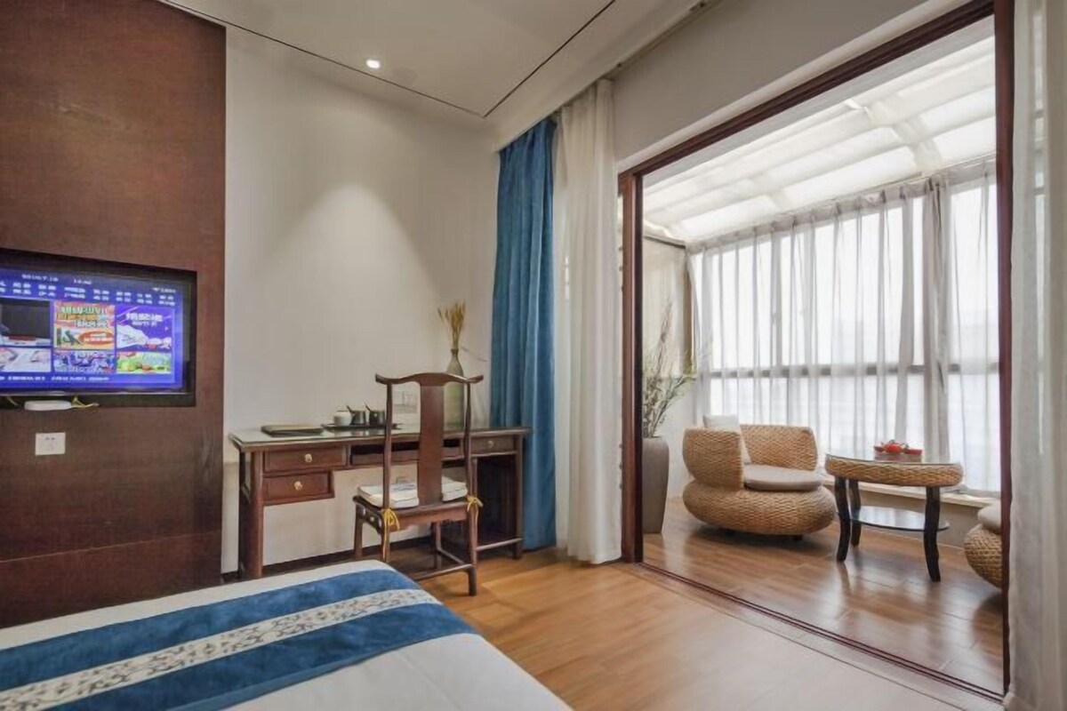 Ein Hotelzimmer mit Bett, Schreibtisch, Stuhl, Fernseher und einem großen Fenster mit Vorhängen.