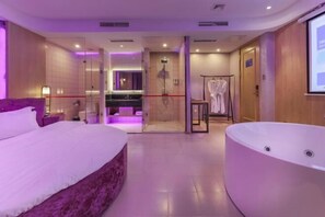 Ein modernes Hotelzimmer mit einem großen Bett, einem separaten Badezimmer, einer bodengrauen Dusche und einer freistehenden Badewanne.