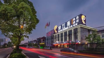 Un hotel con un letrero llamativo, fachada bien iluminada y una calle bordeada de árboles.
