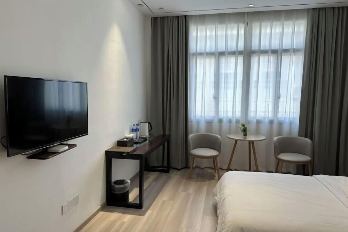 Ein Hotelzimmer mit Flachbildfernseher, Schreibtisch mit Kaffeemaschine, zwei Stühlen, einem kleinen Tisch und einem Bett.