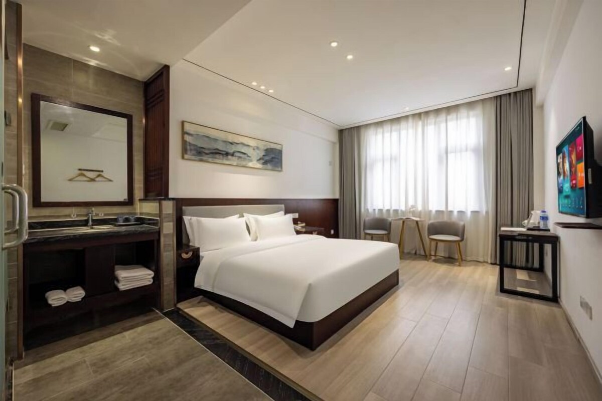 Habitación de hotel con una cama grande, un escritorio con silla, un baño con espejo y un cuadro en la pared.