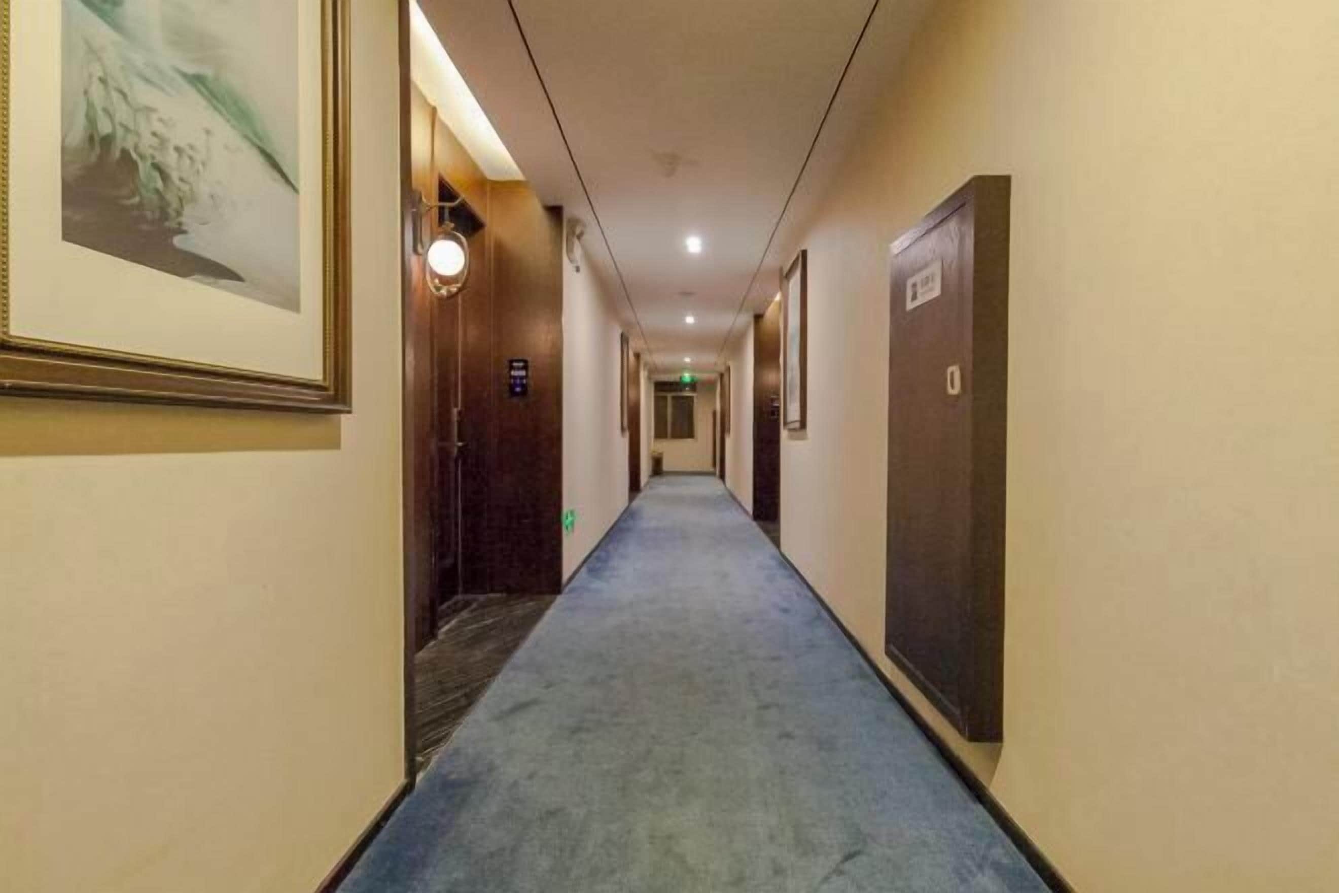 A hotel hallway with a carpeted floor, framed pictures on the walls, and doors on both sides.