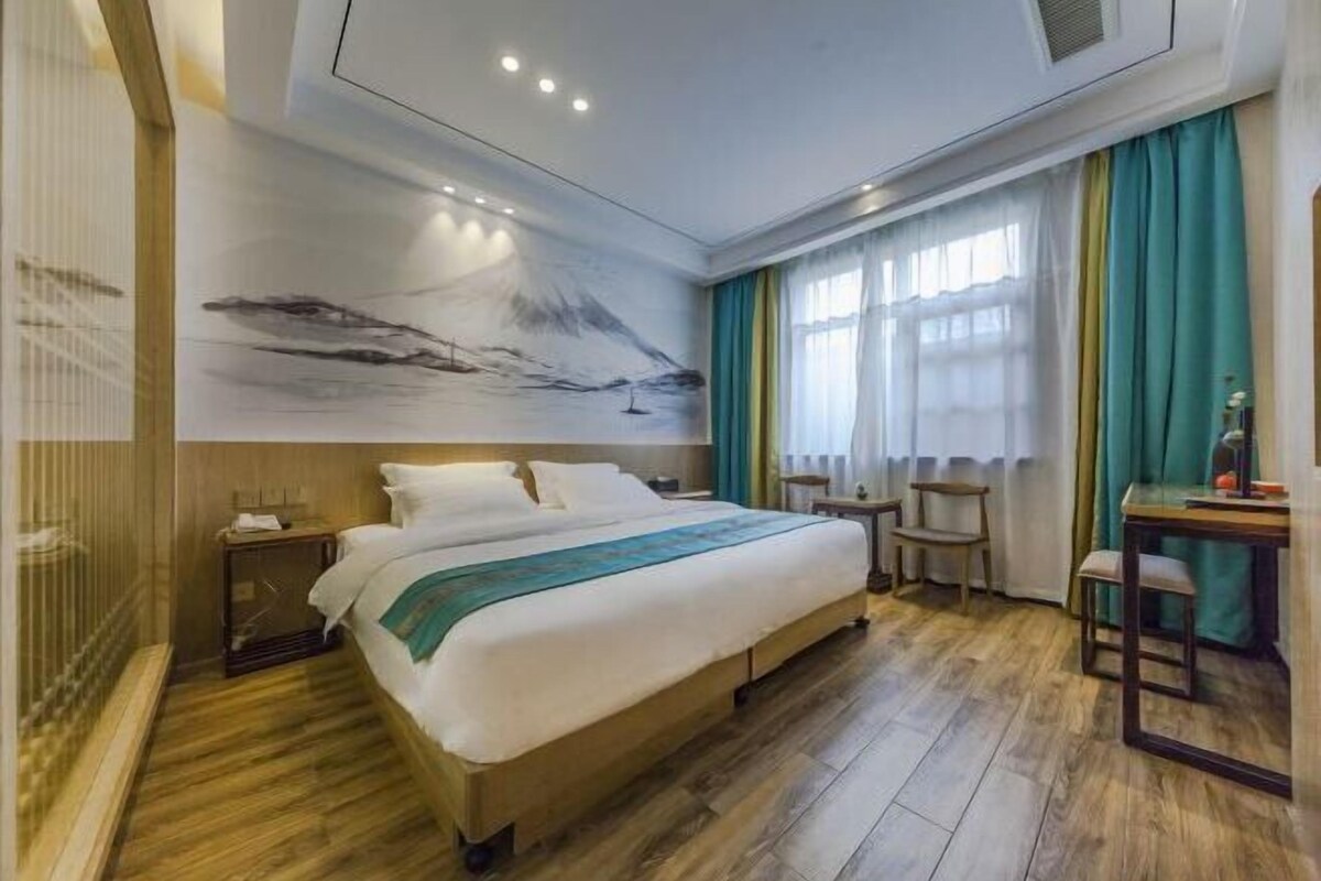 Ein Hotelzimmer mit einem großen Bett, einem Schreibtisch, einem Sessel, einem Nachttisch und einem Wandgemälde.