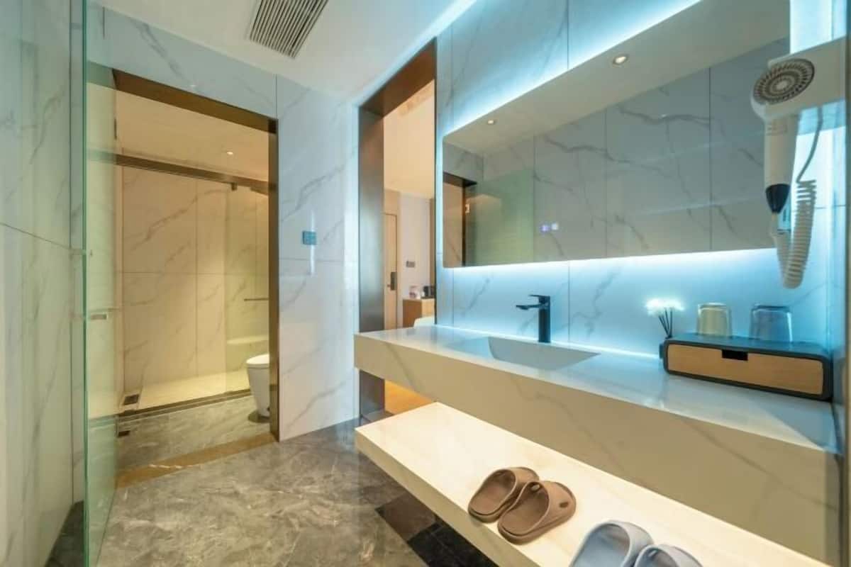 Un baño moderno con suelo de mármol, cabina de ducha de vidrio, un espejo grande y toallero empotrado.