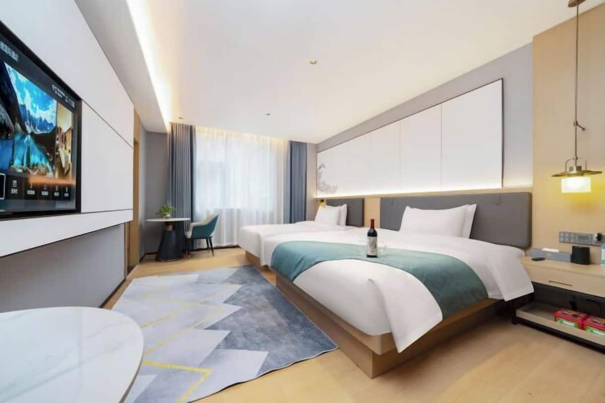 Una habitación de hotel moderna con una cama grande, un televisor montado en la pared, una mesita y una mesilla de noche con lámpara.