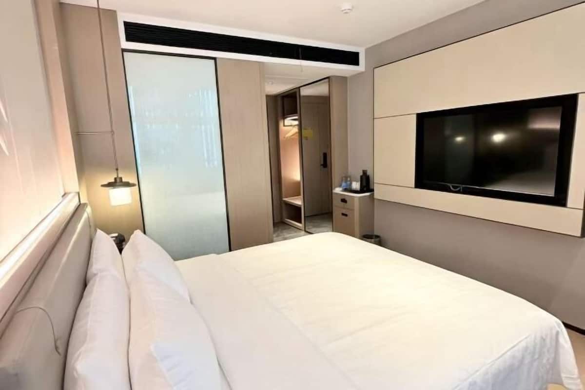 Habitación de hotel con cama, televisor montado en la pared, armario y mesita de noche.