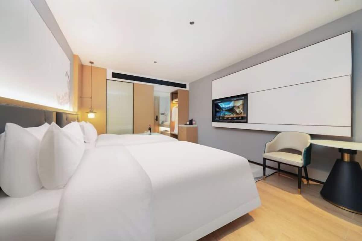 Una habitación de hotel moderna con una cama grande, un televisor de pantalla plana montado en la pared, un escritorio con una silla y un ventanal amplio.