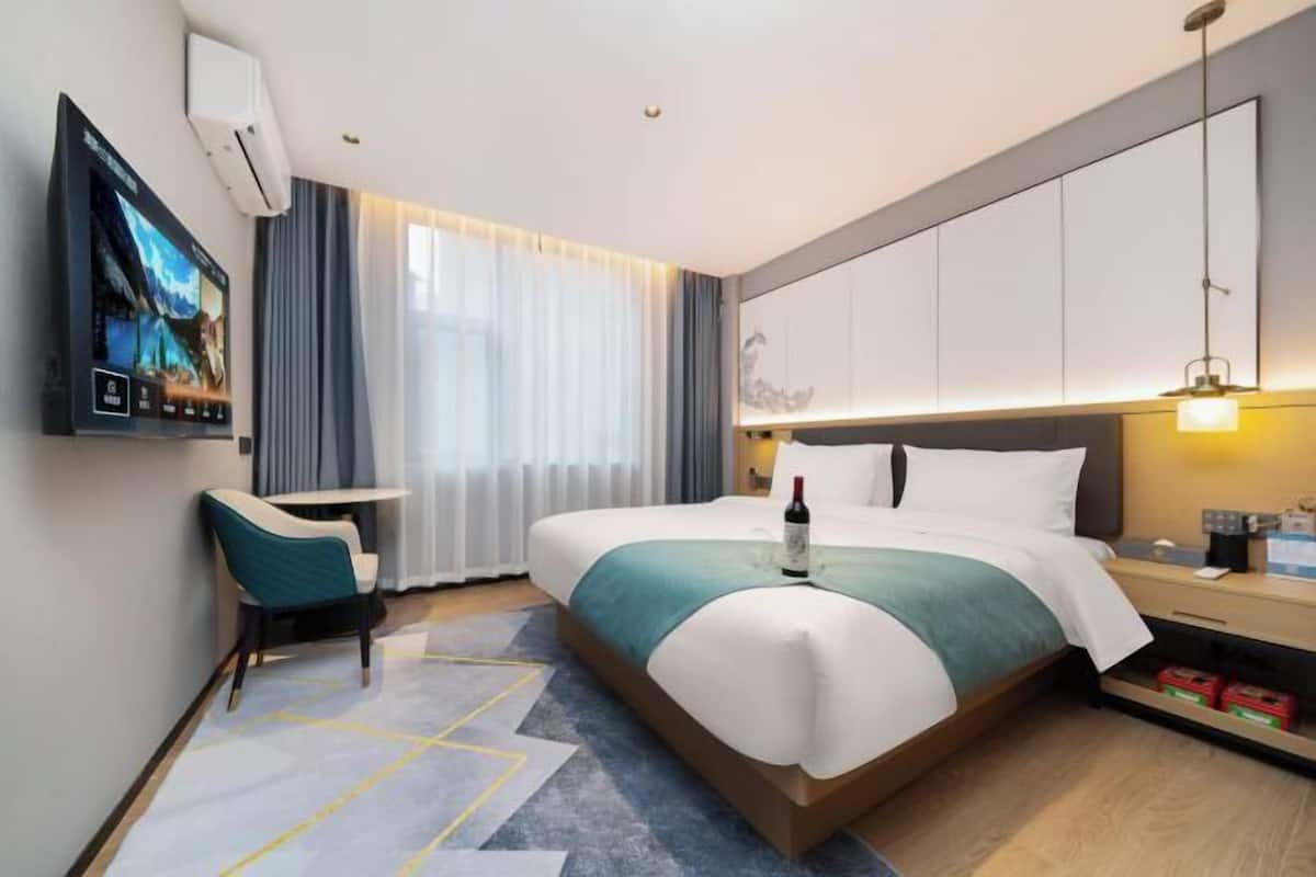 Habitación de hotel con una cama grande, un televisor montado en la pared, un escritorio con una silla y una ventana con cortinas.