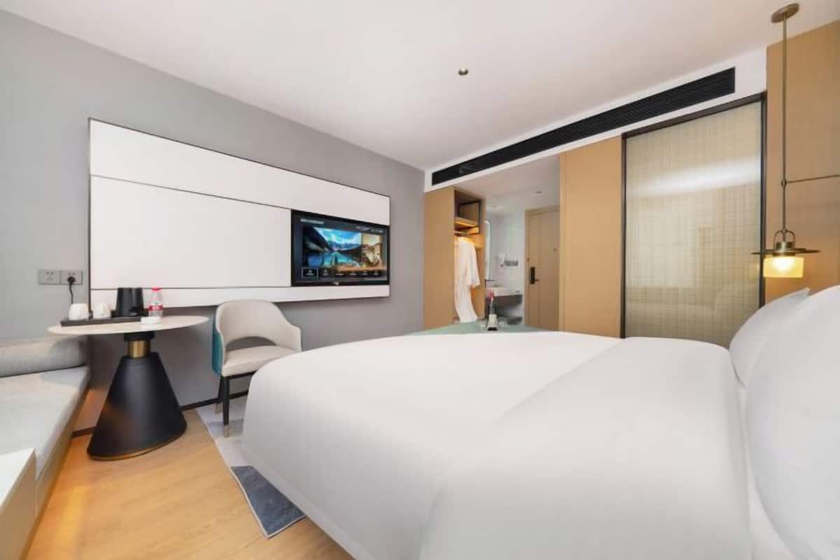 Una habitación de hotel moderna con una cama grande, un televisor, una mesita y una silla.