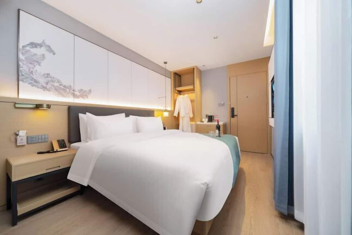 Habitación de hotel con cama, mesita de noche, televisor de pared y una obra de arte grande.