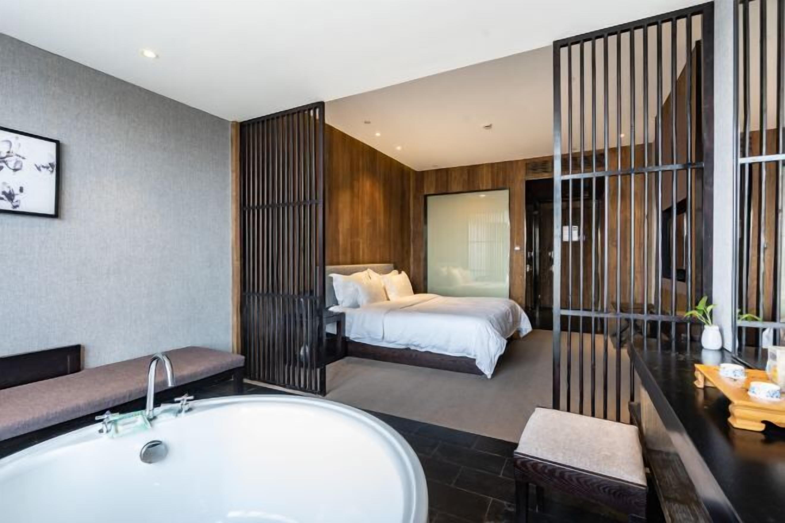 Een moderne slaapkamer met een groot bed, een aparte badkamer met bad en een houten scheidingswand.