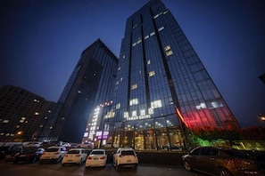 A high-rise building with a glass facade, multiple floors, and a parking area in front. - Tonglu Daman Hotel (Fuchunjiang , Tonglu City Center, Hangzhou) (Tonglu)