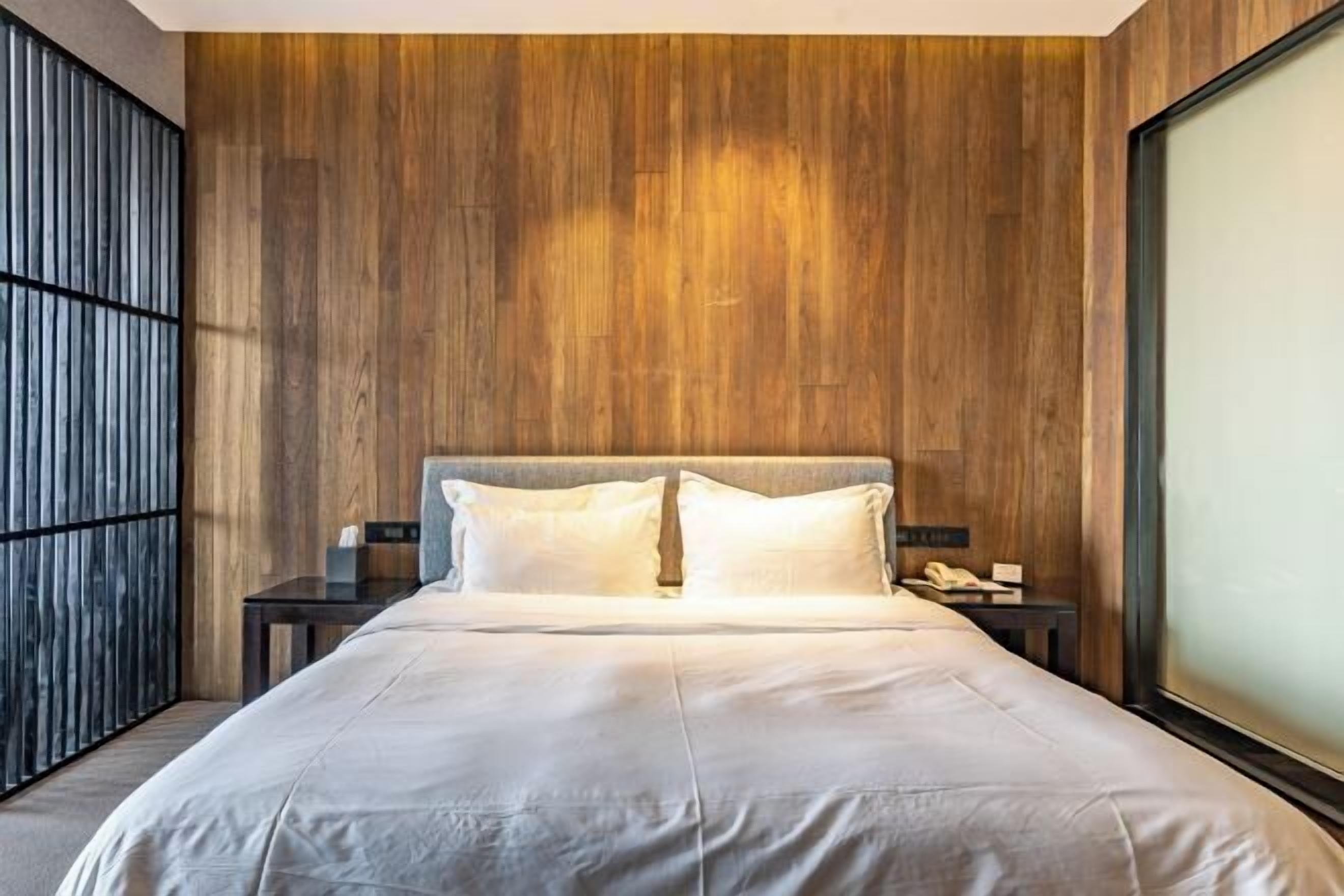 Una habitación de hotel moderna con una cama grande, paneles de madera y un ventanal amplio.
