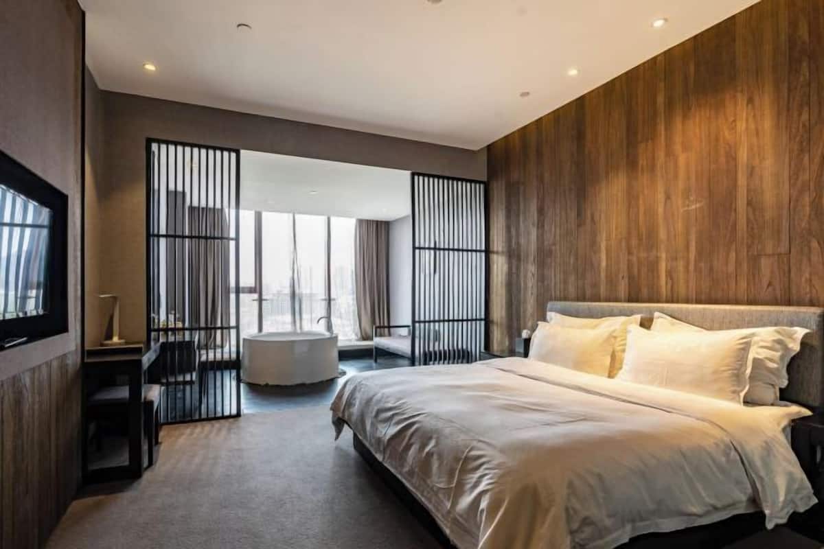 A modern bedroom with a large bed, a desk, and a bathtub.