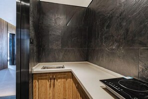 A modern kitchen with dark stone walls, a wooden cabinet, and a built-in induction cooktop.