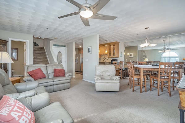 A spacious living room with a large sectional sofa, a dining area with a wooden table and chairs, and a ceiling fan.