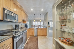 A modern kitchen with wooden cabinets, stainless steel appliances, a dishwasher, and a glass display shelf with glassware.