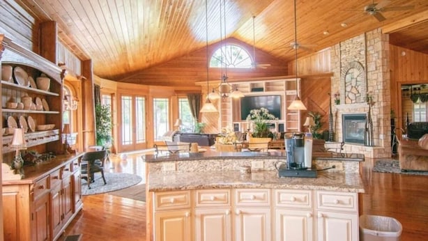 A spacious kitchen with wooden cabinets, a large island, and a stone fireplace.