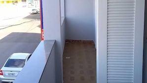 Un pasillo estrecho con pared blanca, suelo de baldosas y una puerta blanca cerrada con listones horizontales.
