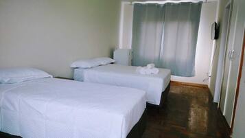 Habitación de hotel con dos camas individuales, una mesita con toallas, un televisor y una ventana con cortinas.