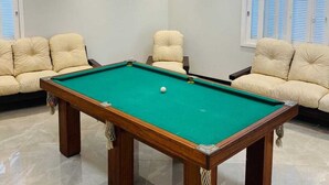 Una mesa de billar en una habitación con dos sofás color crema y una lámpara en el techo.