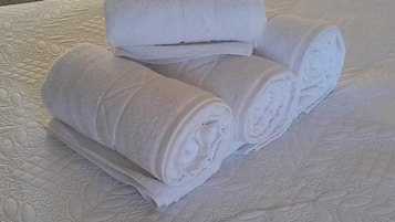 Toalhas brancas dobradas com cuidado, empilhadas sobre um cobreleito branco texturizado.