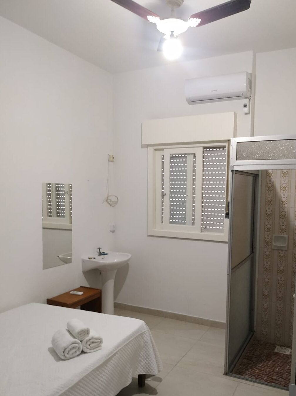 A small, clean room with a bed, a sink, a mirror, and a shower.