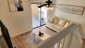 Una sala de estar con sofá, una mesa de centro, una lámpara de pie y un cuadro en la pared.