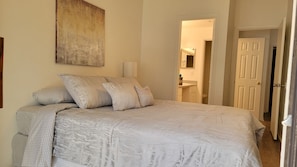 A bedroom with a large bed, a bedside table, a wall-mounted lamp, and a door leading to a bathroom. - Tranquil Townhouse 🏡💤 - A peaceful retreat that promises restful slumber (Gainesville)