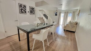Un espacio habitable moderno con una mesa de comedor de vidrio, sillas blancas, una escalera y un sofá.