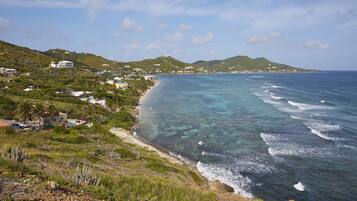 A coastal landscape with a clear view of the ocean, a beach, and a hillside with buildings.