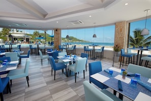A restaurant with outdoor seating overlooking the beach, featuring blue chairs and tables, and a view of the ocean. - Oceans at Carina Bay Adults Only (Christiansted)