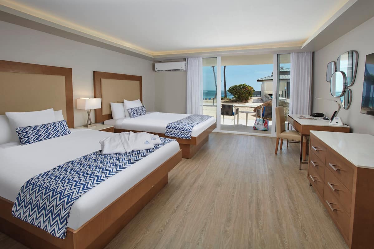 Een hotelkamer met twee bedden, een bureau en uitzicht op het strand.
