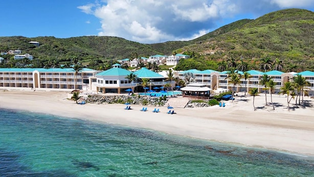 A beachfront hotel with multiple buildings, a sandy beach, and a clear view of the ocean.