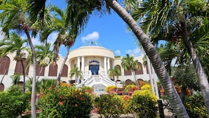 A building with a dome and columns, surrounded by palm trees and a garden with red flowers.