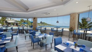 A restaurant with outdoor seating overlooking the beach, featuring blue chairs and tables, and a view of the ocean.
