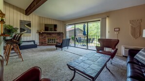 Ein Wohnzimmer mit Kamin, einer Essecke mit Tisch und Stühlen sowie Blick ins Freie durch große Schiebeglastüren.