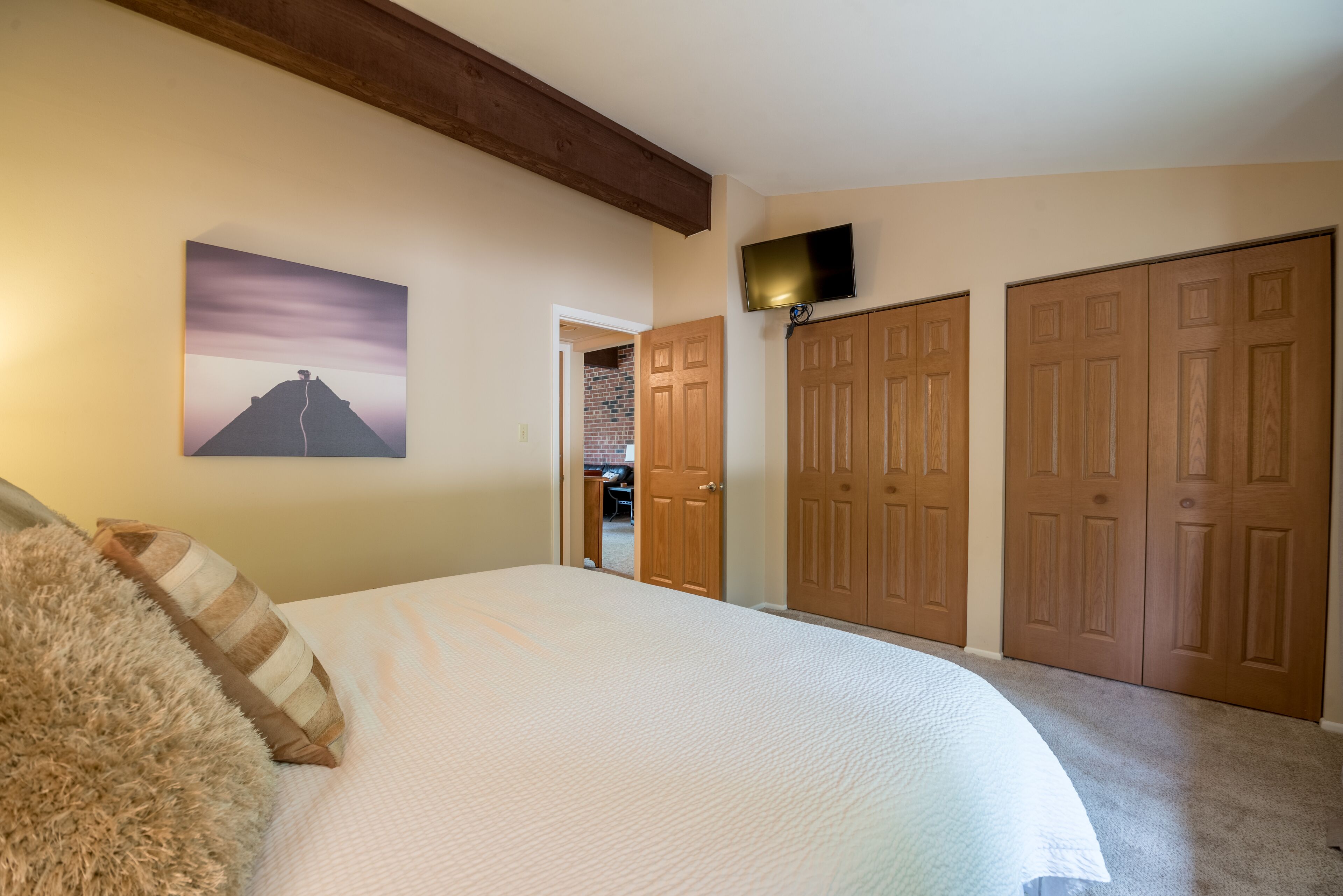 A bedroom with a large bed, wooden doors, a TV, and a painting on the wall.