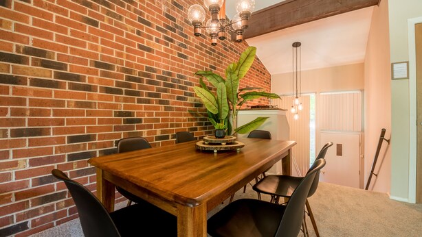 Ein Essbereich mit Backsteinwand, Holztisch, schwarzen Stühlen und einem Blumentopf.