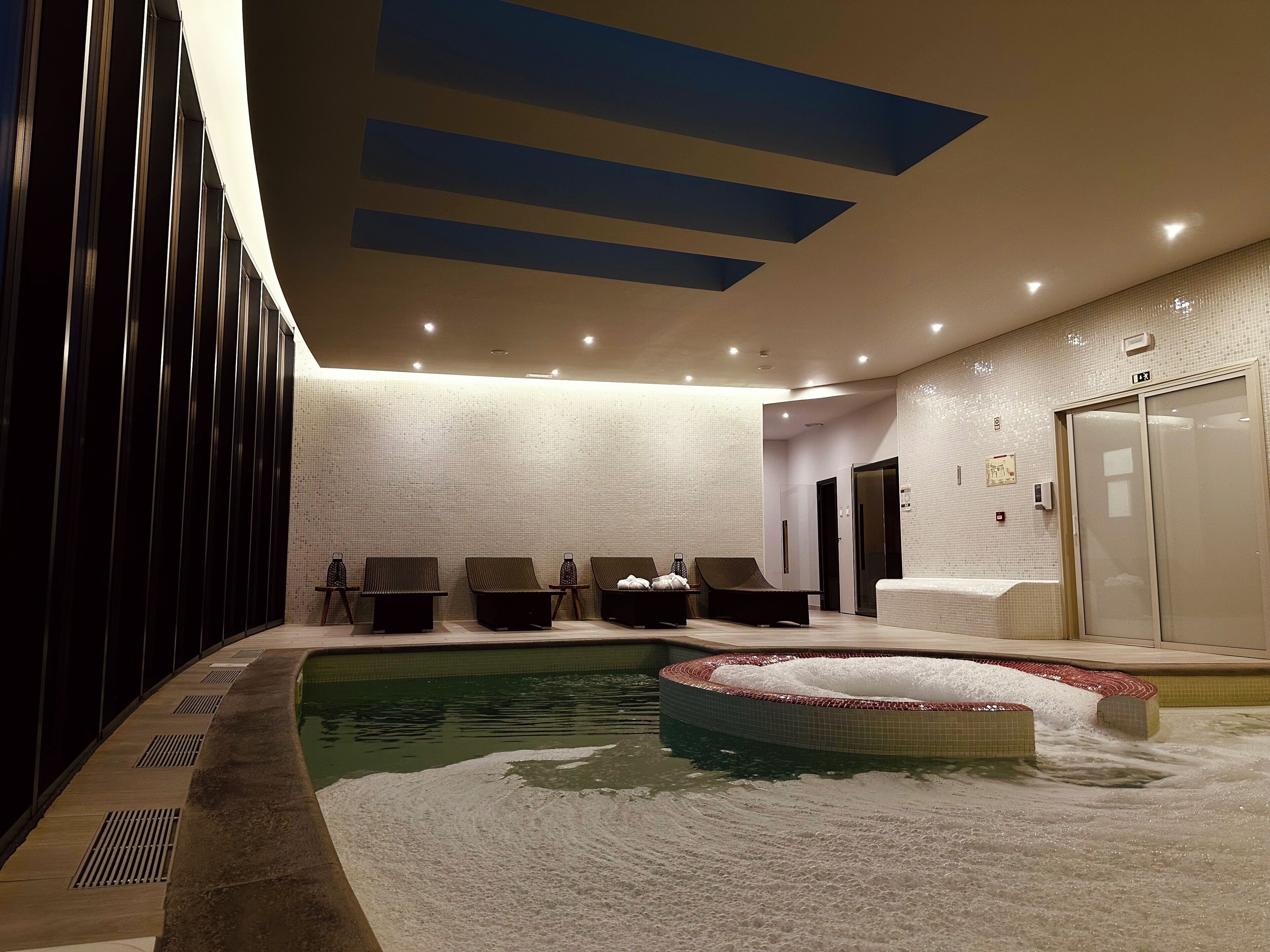 Zona de spa con bañera de hidromasaje, sillas de descanso y pared de azulejos.