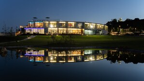 A modern building with a glass facade, a reflection in the water, and a well-maintained lawn. - Grapple Hotel (Carrazeda de Ansiaes)