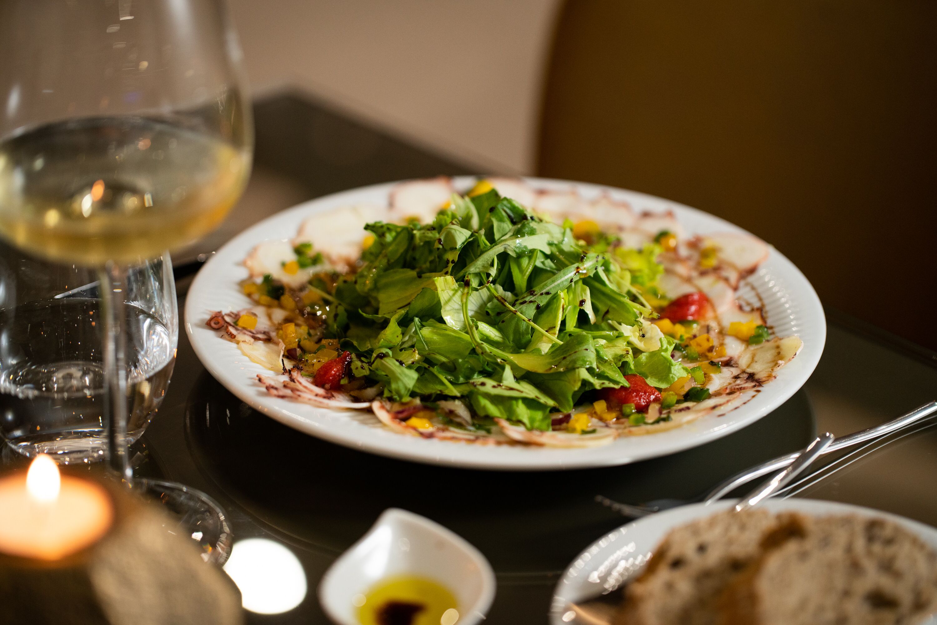 A plate of salad with a glass of white wine on a table.