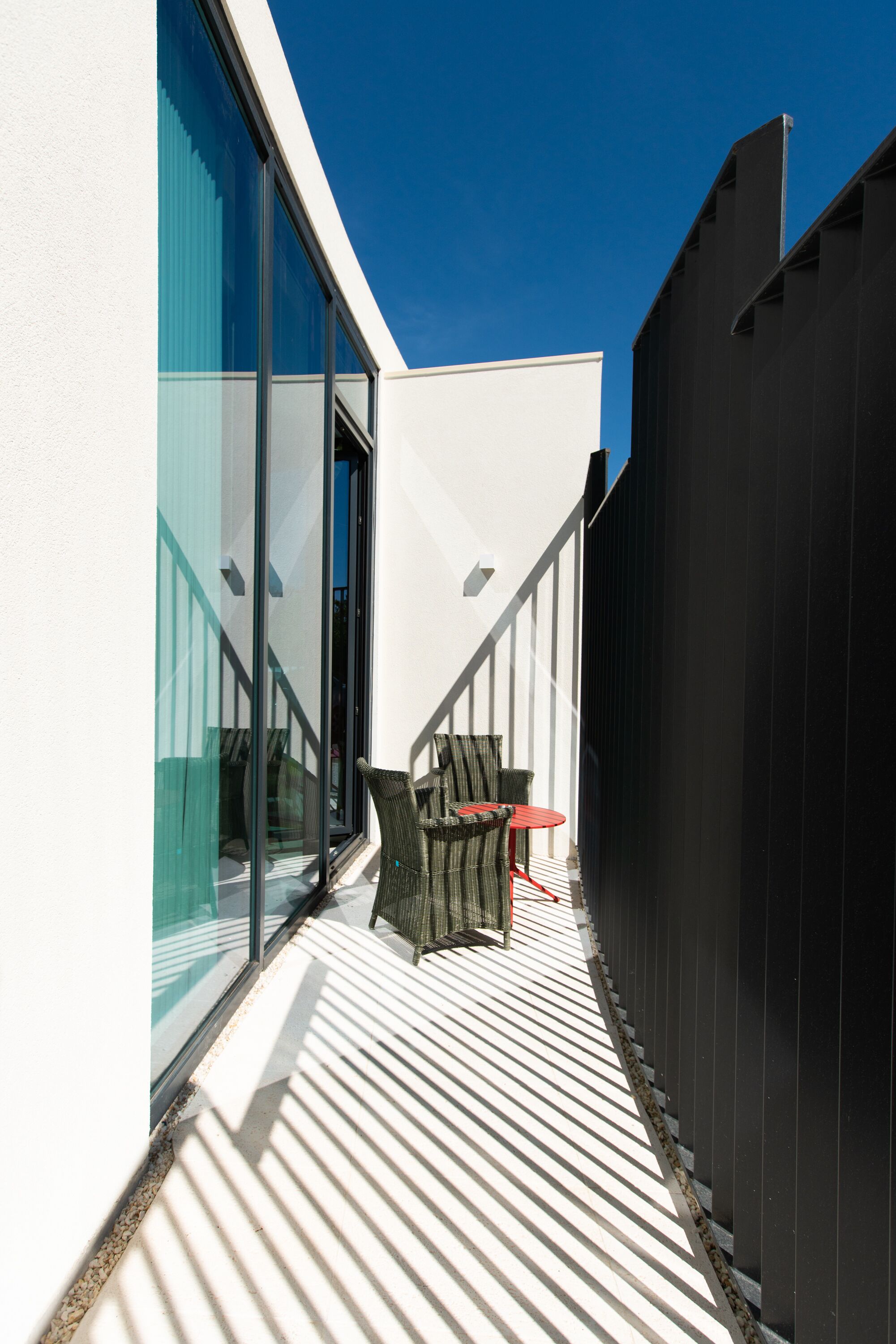 Ein Balkon mit weißer Brüstung, einer Glastür und einem roten Tisch.