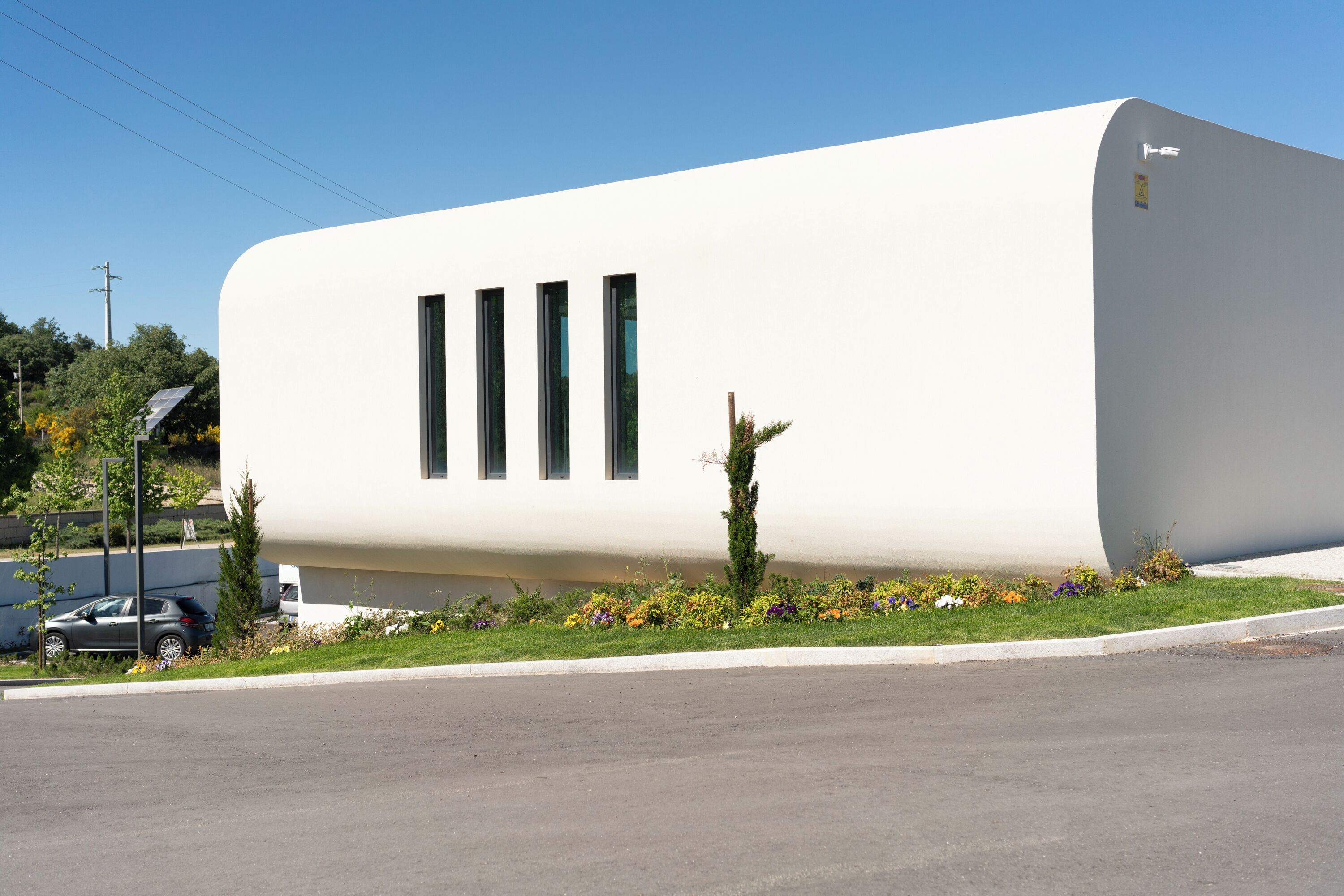 A modern building with a white facade, three vertical windows, and a curved corner.