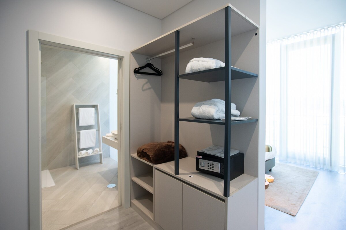A modern bathroom with a glass shower enclosure, a white towel rack, and a built-in shelving unit with towels and a brown item.