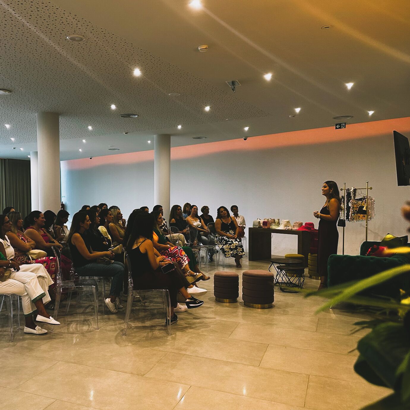 Un salón de conferencias con un orador al frente, asistentes sentados en sillas y una exhibición de objetos sobre una mesa.