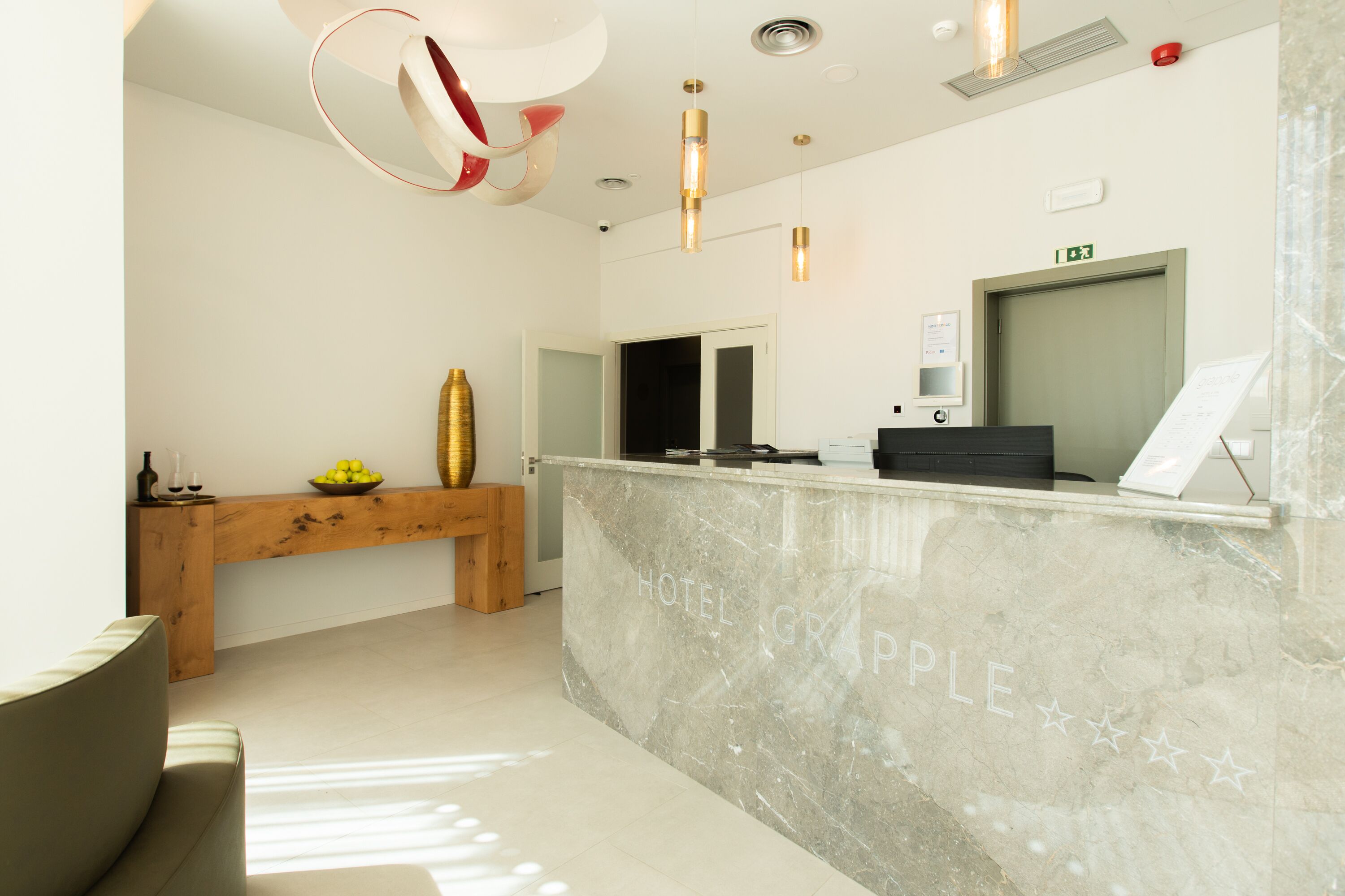 Zona de recepción de un hotel con mostrador de mármol, banco de madera e iluminación moderna.