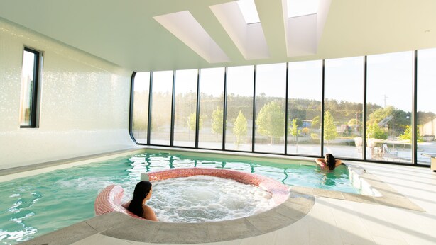 An indoor swimming pool with clear views of the outdoors, large windows, and a tiled floor. - Grapple Hotel (Carrazeda de Ansiaes)