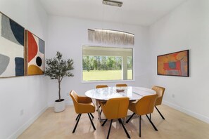 Un comedor moderno con una mesa redonda, seis sillas, una planta en maceta y obras de arte en las paredes.